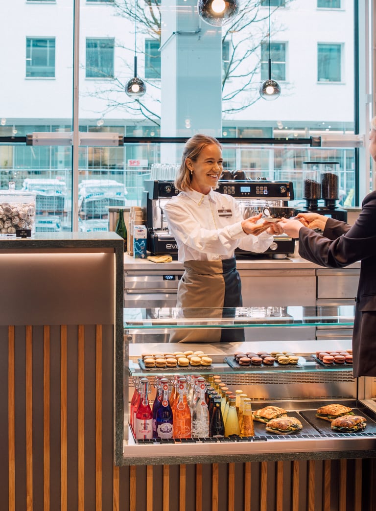 Kundin wird in einem Café bedient, Stadtansicht im Hintergrund.