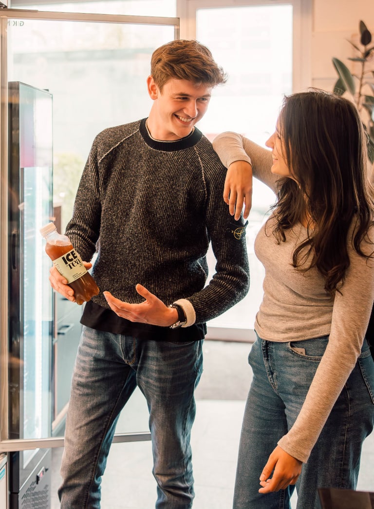 Zwei Personen stehen lächelnd vor einem offenen Kühlregal mit Getränken.