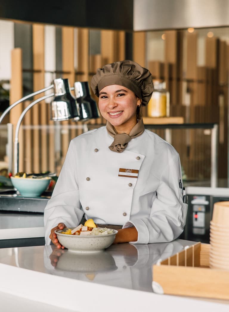 Köchin in weissem Mantel mit Essensschale am Restauranttresen.
