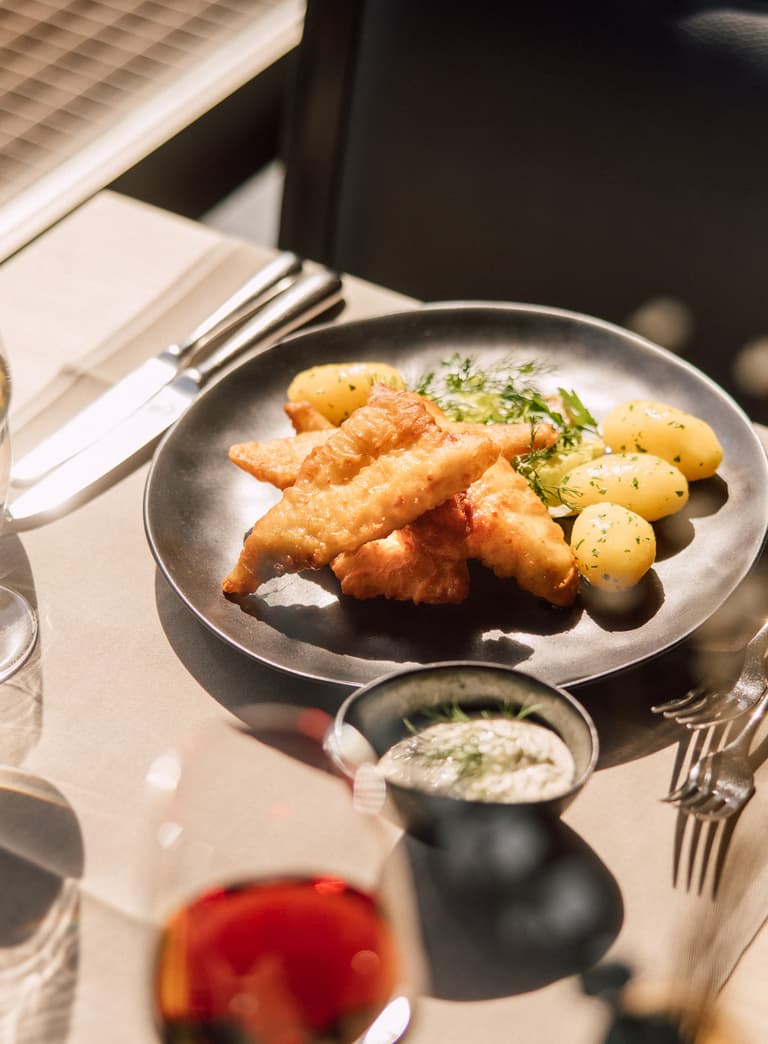 Gebratener Fisch mit Kartoffeln auf einem Teller, Wein und Wasser im Glas.