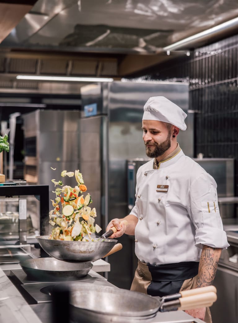 Koch in Restaurantküche wirft Gemüse in der Pfanne.