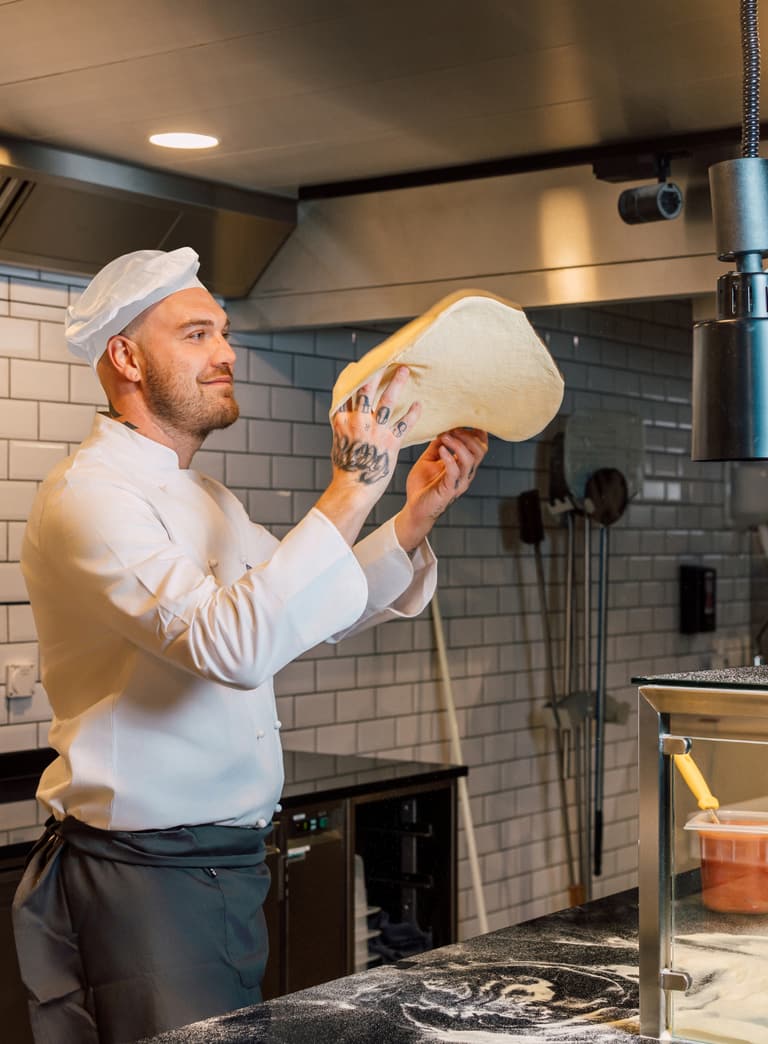Koch mit Teig in einer Pizzeria-Küche.