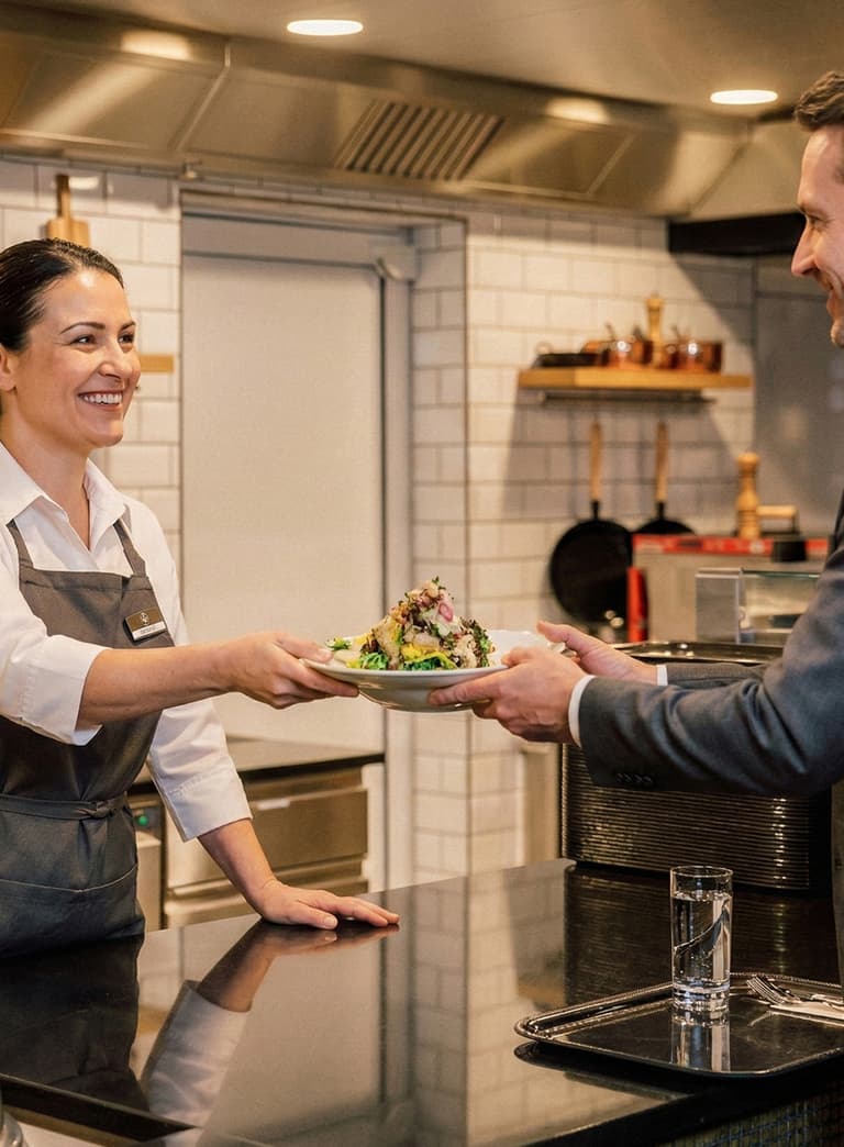 Kellnerin überreicht einem Mann Teller mit Essen in Restaurantküche.
