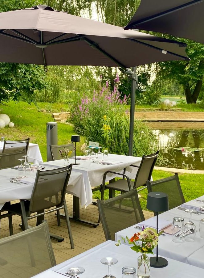 Gedeckte Aussenterrasse mit Teich und Sonnenschirmen.