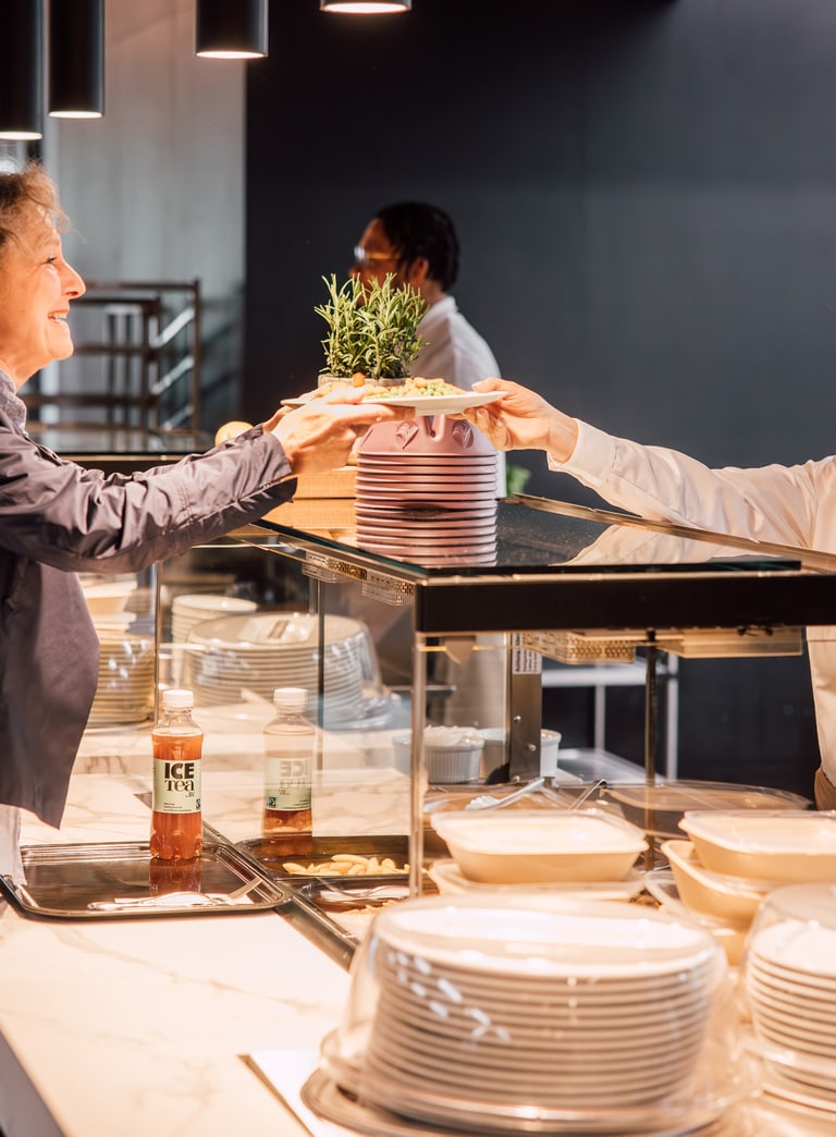 Zwei Frauen geben sich an einem Restaurantbuffet eine Pflanze.