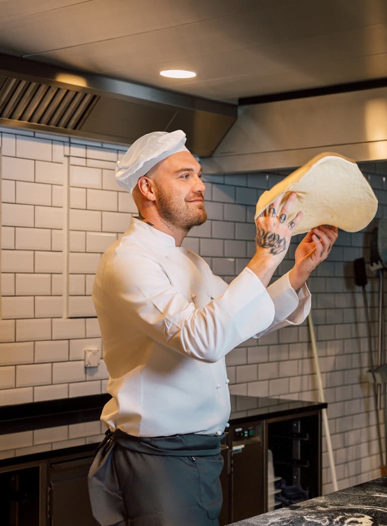 Koch wirft Pizzateig in der Küche in die Luft.