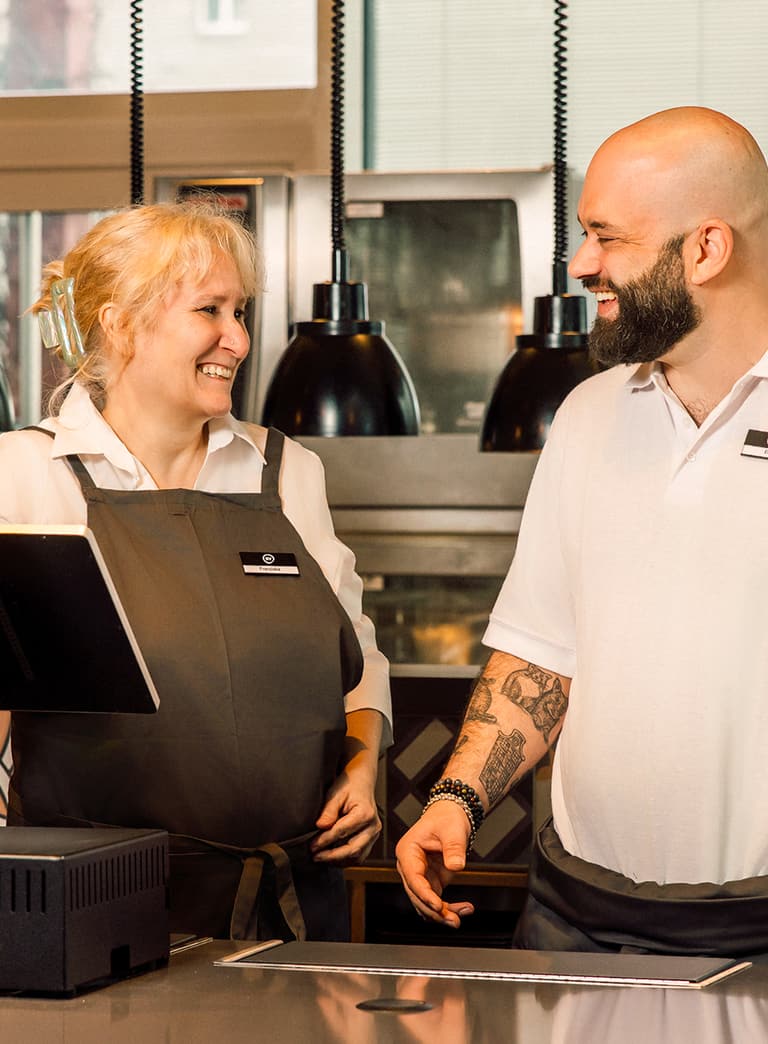 Zwei lächelnde Mitarbeiter im Restaurant hinter der Theke.
