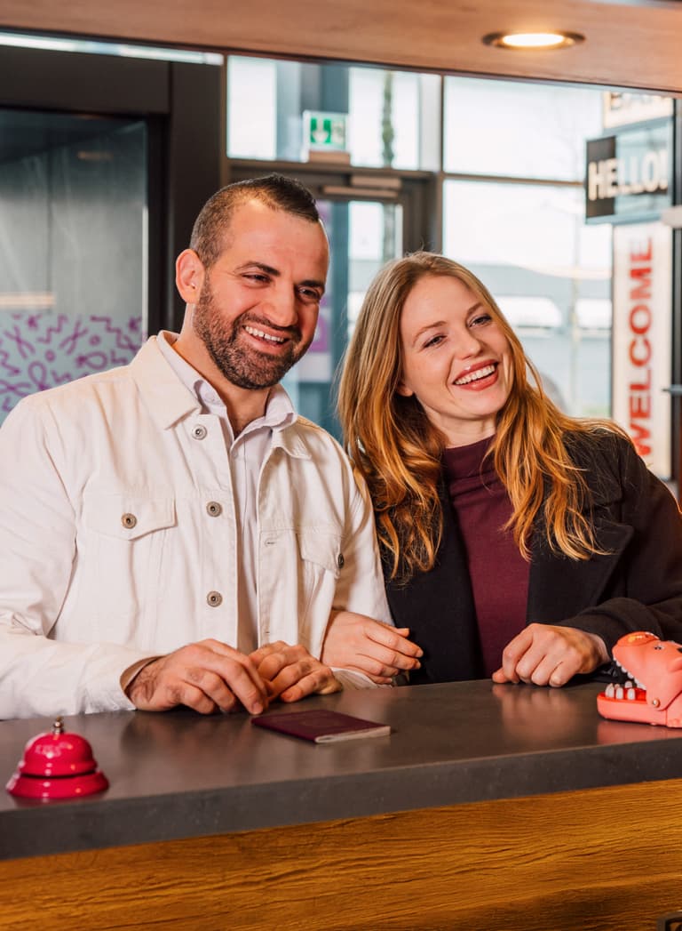 Paar lächelt an der Rezeption eines Hotels.