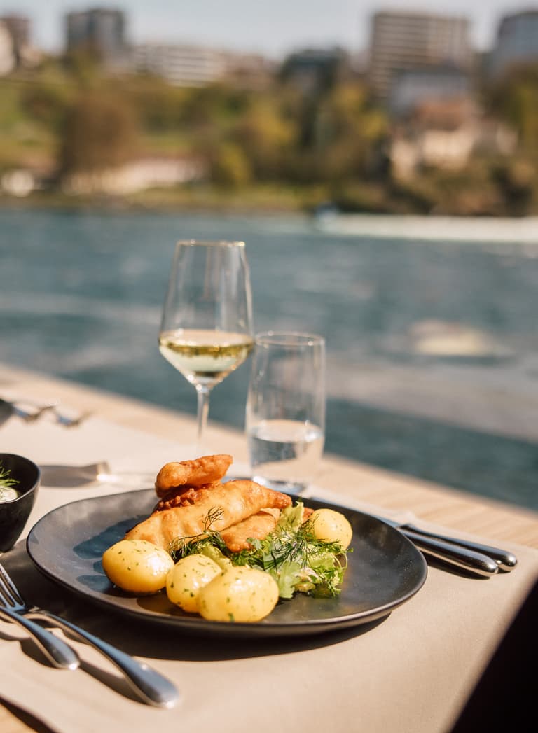 Tisch mit Essen und Weingläsern am Flussufer.