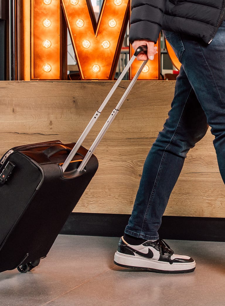 Person zieht Rollkoffer neben leuchtenden Buchstaben vorbei.