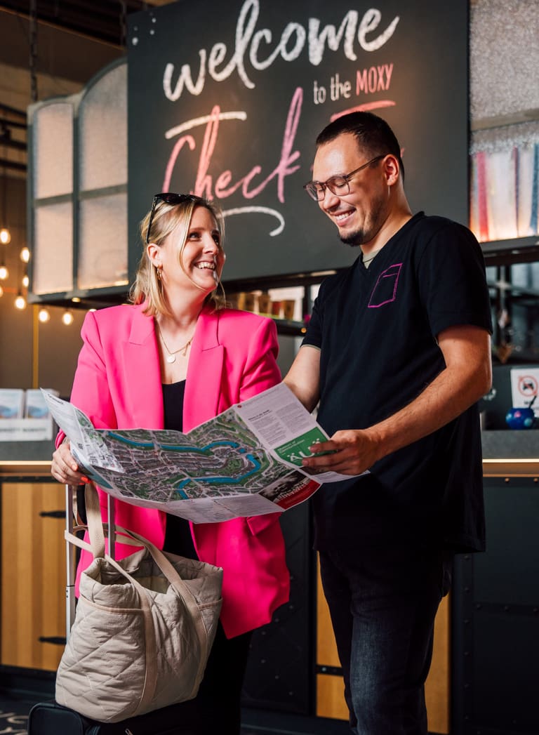 Zwei Personen mit Karte vor Rezeption des Moxy Hotels.