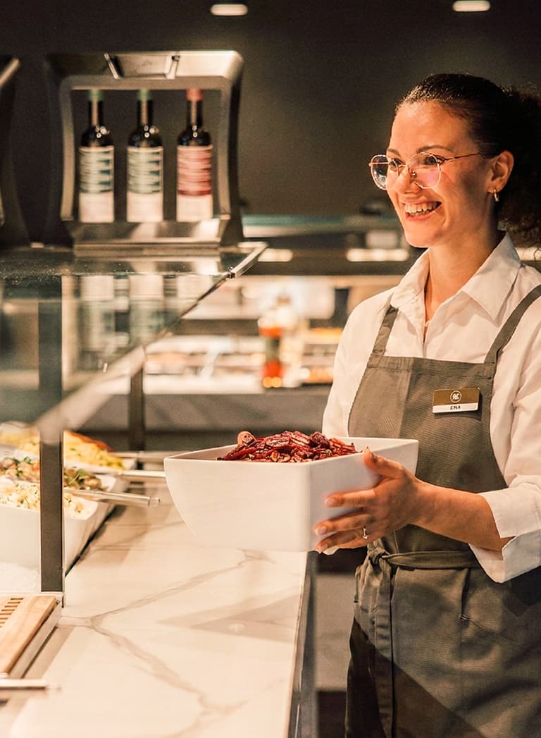 Lächelnde Frau mit Schüssel an Salatbuffet.