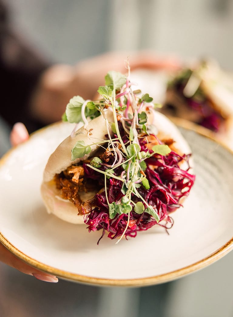 Person hält Teller mit gefülltem Bao-Brötchen und Kräutern.