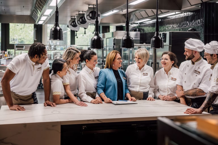 Gruppe von Köchen und Servicepersonal, die in einer Restaurantküche kommunizieren.