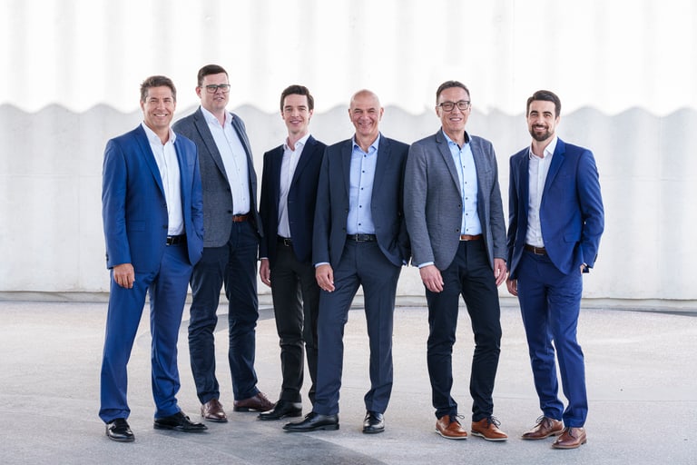 Sechs Männer in Business-Kleidung stehen nebeneinander.