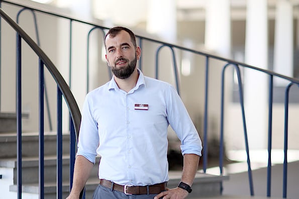 Mann in weissem Hemd und grauen Hosen steht auf einer Treppe.",