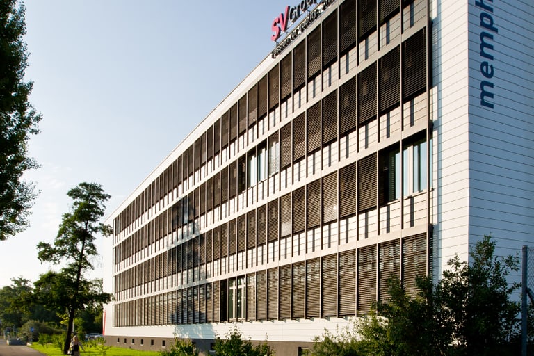 Modernes Bürogebäude mit Glasfassade und Firmenlogos am Tag.