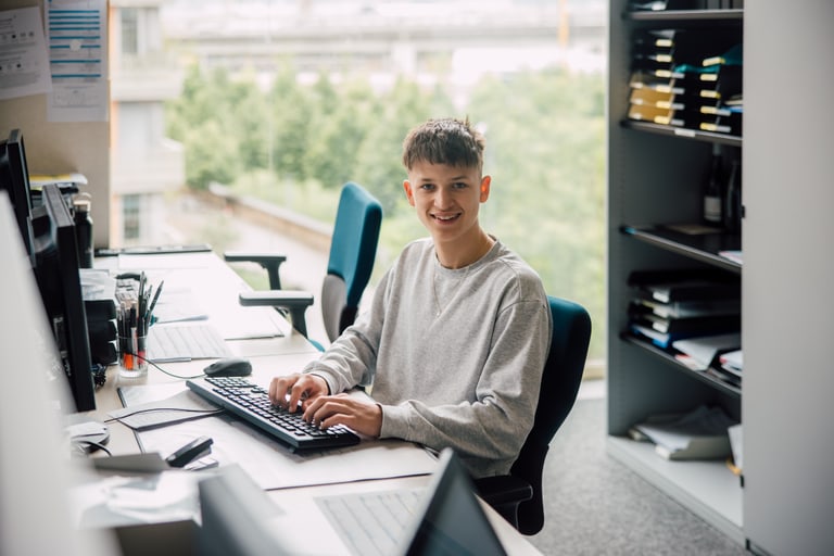 Junger Mann sitzt am Schreibtisch mit Computern im Büro.
