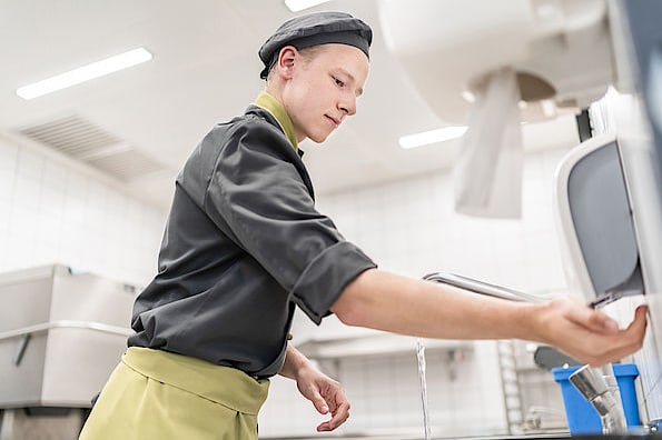 Mitarbeiter in der Küche wäscht seine Hände nach den SV Hygienevorschriften.