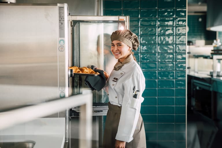 Köchin nimmt Croissants aus dem Ofen in der Küche heraus.