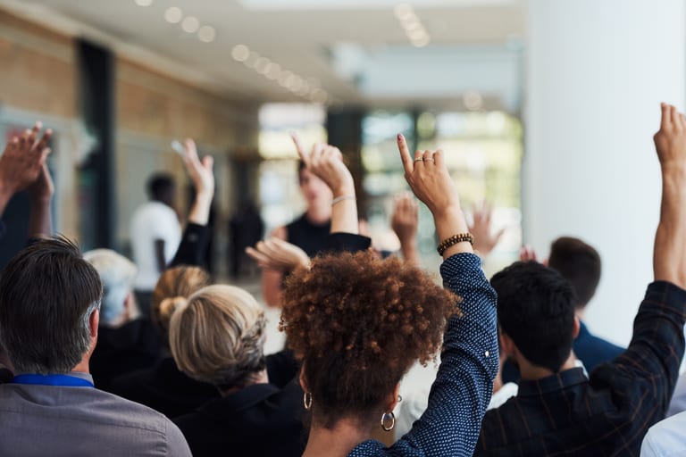Menschen mit erhobenen Händen bei einer Veranstaltung in einem modernen Raum.