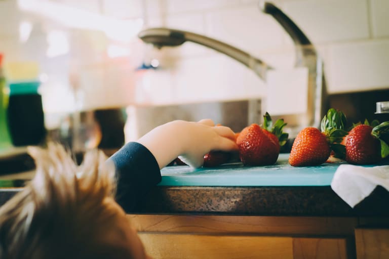 Kind greift nach Erdbeeren auf Küchenarbeitsplatte.