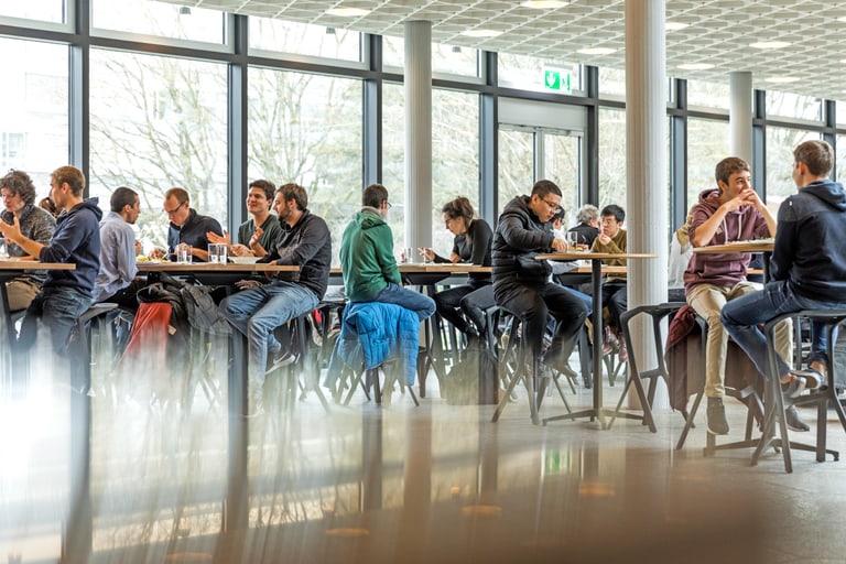 Studentinnen und Studenten sitzen in der hellen und modernen Mensa und geniessen ihr Mittagessen.