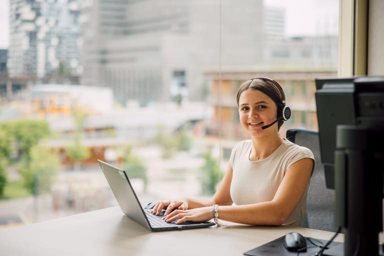 Frau mit Headset arbeitet am Laptop im Büro.