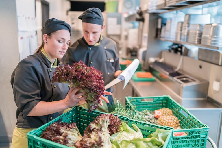 Zwei Mitarbeitende in der Küche kontrollieren die Lieferung von frischen Zutaten wie Salat und Früchten.