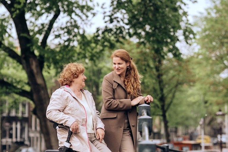 Ältere Frau mit Rollator und junge Frau gehen an einem Kanal entlang.
