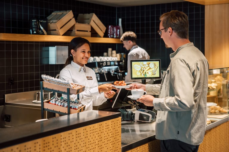 Kundenservice in einem Café mit Barista und Kunde am Tresen.