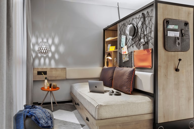 Modern eingerichtetes kleines Hotelzimmer mit Einzelbett, Arbeitsbereich und Dekoration.