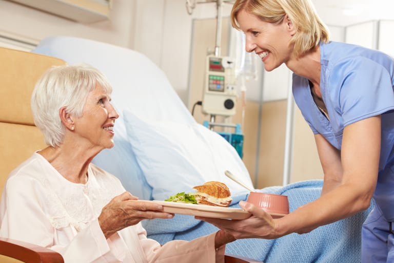 Krankenschwester serviert älterer Patientin im Krankenhauszimmer Essen.