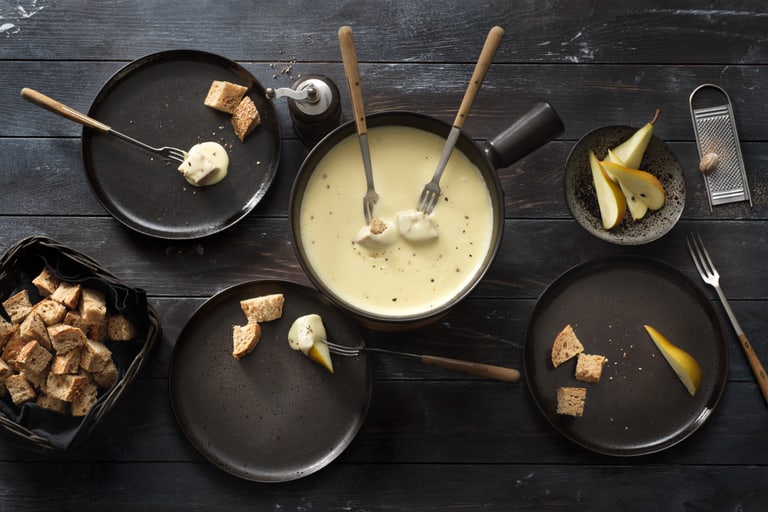 Käsefondue mit Brot und Birne auf Holztisch.