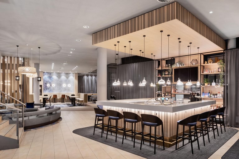 Eine elegante und moderne Bar mit einer Lounge im Eingangsbereich eines Hotels mit viel Licht und hellem Holz.