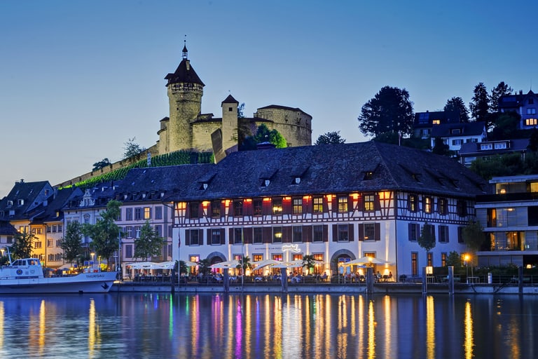 Aussenansicht des Güterhofs Schaffhausendirekt am Rhein in der Dämmerung schön beleuchtet und im Hintergrund der Munot.