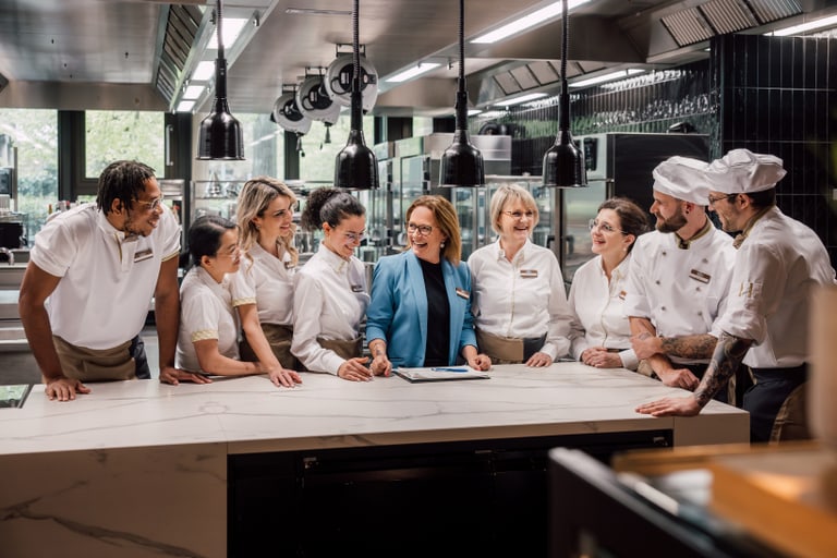 Gruppe von Köchen und Servicepersonal bespricht Pläne in einer Restaurantküche.