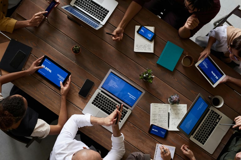 Personen sitzen an einem Tisch bei einem Meeting und haben ihre Laptops geöffnet.