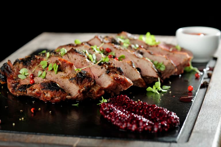 Gegrilltes Fleisch mit Kräutern und Sauce auf Holzbrett serviert.