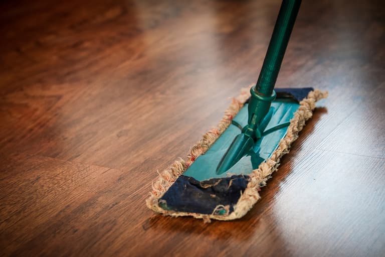 Grüner Bodenwischer auf Holzboden.",