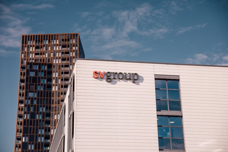 Bürogebäude mit SV Group-Logo vor einem Hochhaus.",