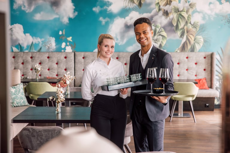 Zwei Kellner mit Tabletts in einem stilvoll dekorierten Restaurant.