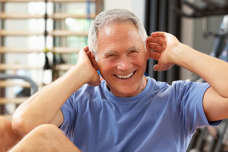 Älterer Mann lächelt beim Training im Fitnessstudio.