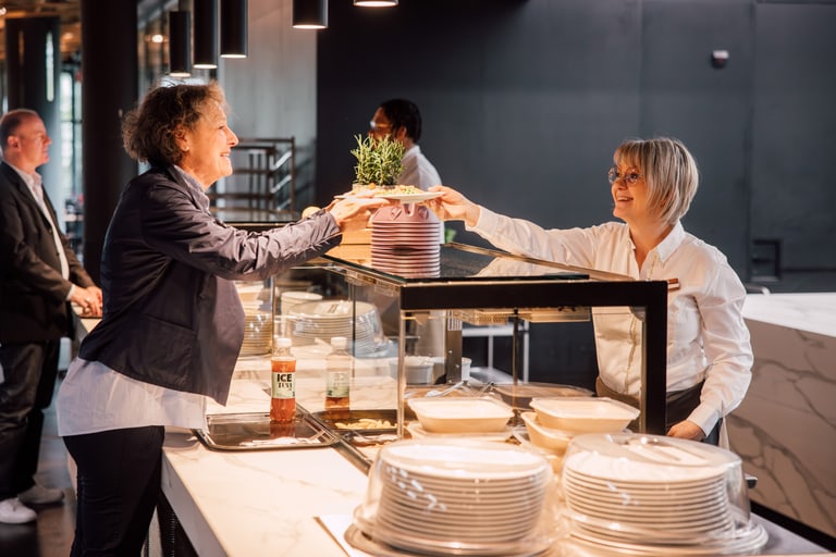 Zwei Frauen geben sich an einem Restaurantbuffet eine Pflanze.