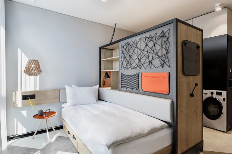 Modernes kompaktes Studio-Apartment mit integriertem Bett, Waschmaschine und Arbeitsbereich.
