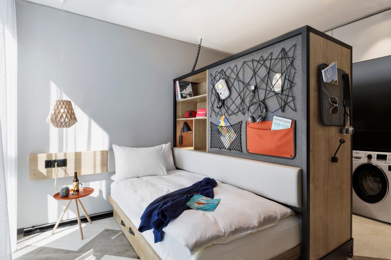 Kleines Schlafzimmer mit Bett, Trennwand und Waschmaschine.