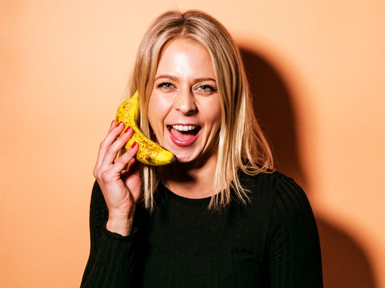 Frau in schwarzem Oberteil hält eine Banane ans Ohr.