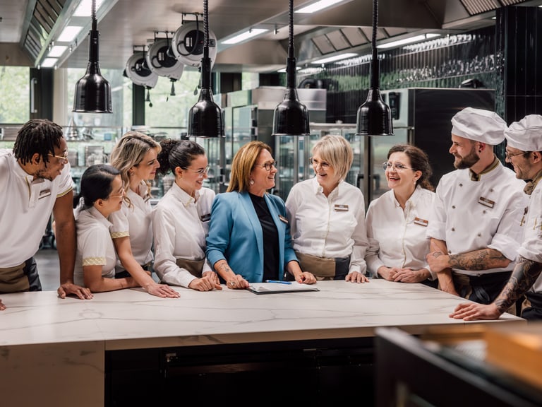 Gruppe von Köchen und Servicepersonal, die in einer Restaurantküche kommunizieren.