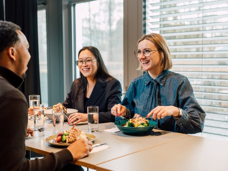 Drei Personen beim Mittagessen in einem Restaurant lächelnd am Tisch.