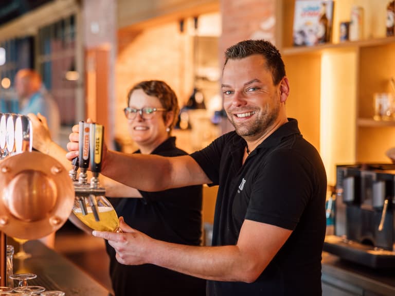 Mann und Frau zapfen Bier an der Theke.